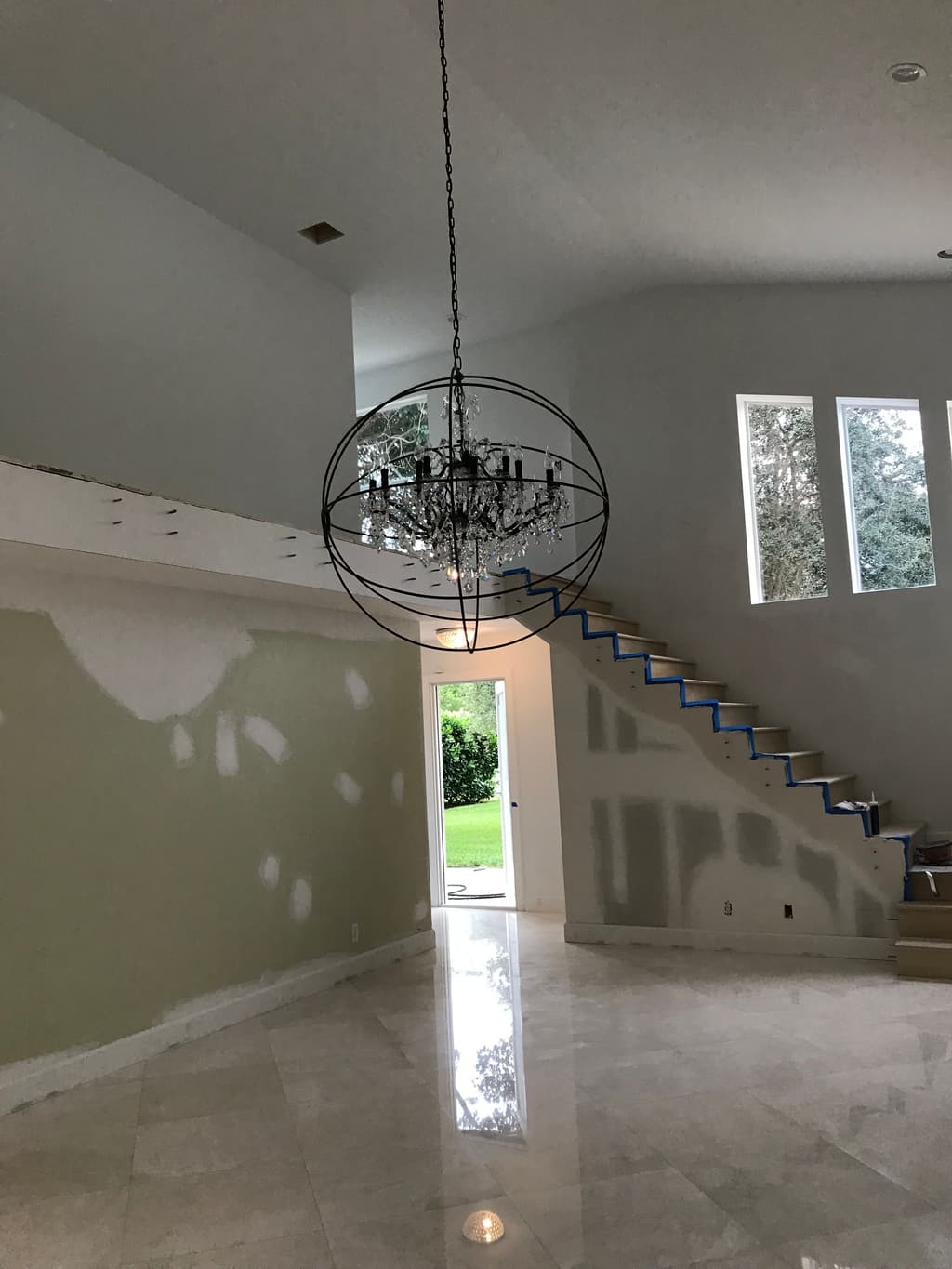 The stair hall with a new open-tread stair, an orb chandelier hung overhead and patched drywall waiting for paint.